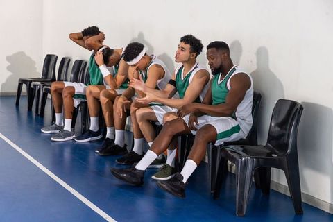 Diverse Basketball Team Resting on Sidelines in Gymnasium