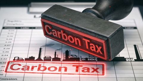 Red carbon tax stamp pressing over industry emissions spreadsheet with factory silhouette