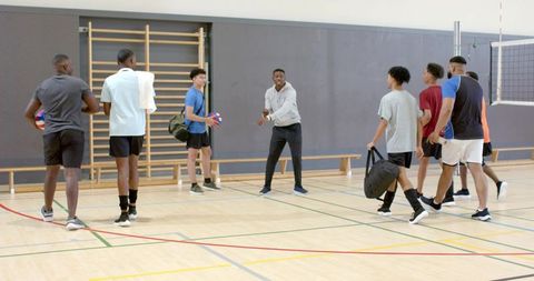 Diverse male volleyball team gathering for training and drills in indoor school gymnasium