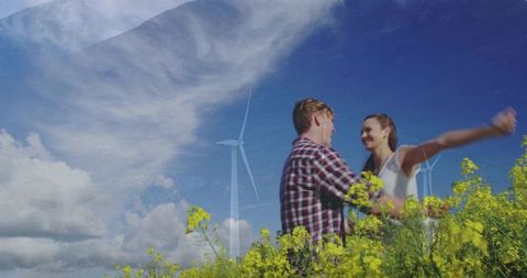 Young couple embracing in canola field with wind turbines and blue sky, sustainable romance