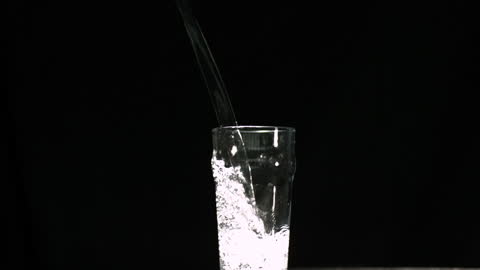 Sparkling water is pouring into a clear glass, creating dynamic movement with bubbling effects against an elegant black background. This visual can be used for illustrating freshness, hydration tips, or advertising beverages. Its simplicity and elegance make it suitable for use in hospitality or wellness content.