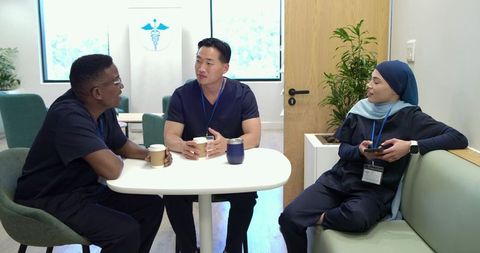 Diverse clinicians sharing coffee and conversation in modern medical breakroom lounge