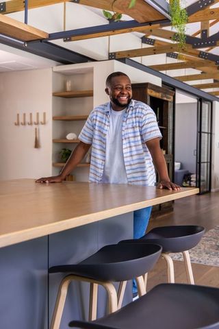 Smiling african american man standing behind wooden kitchen island in modern rustic home
