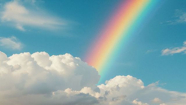 Vibrant rainbow arcing across blue sky with cumulus clouds