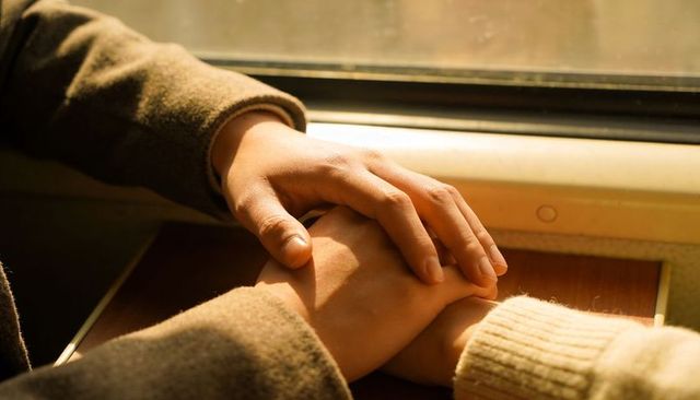 Clasping hands bathing in sunlight on train table conveying warmth and intimacy