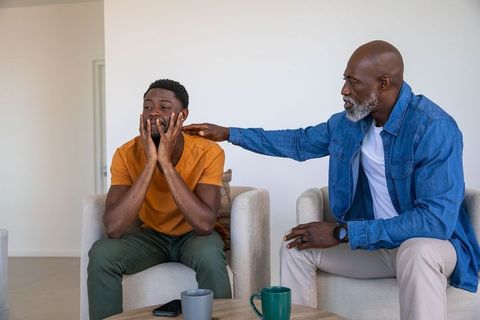 Father consoling adult son in living room