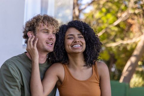 Sunlit mixed couple sharing laughter on porch, affectionate outdoor moment of togetherness