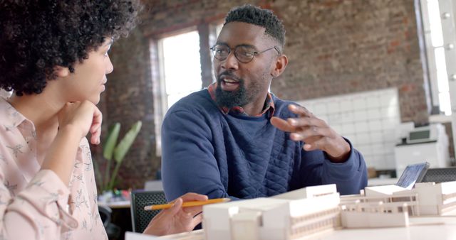 Two architects intently collaborating on a building model in a modern workspace with exposed brick walls. Suitable for representing teamwork, creative processes in architecture, interior design concepts, and professional office settings where collaboration and discussion are paramount.