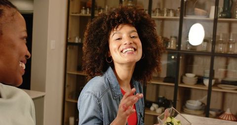 Laughing diverse friends sharing cucumber salad at kitchen counter casual home gathering