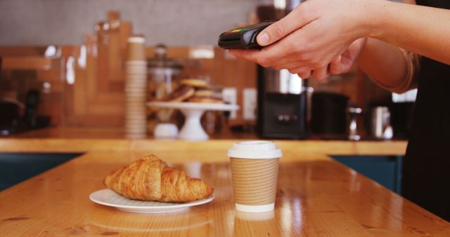 Caucasian female barista using payment terminal over croissant and coffee in cafe. Business, work, drink and cafe, unaltered.
