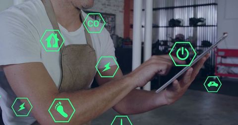 Workshop technician monitoring energy use and co2 footprint on tablet with smart icons