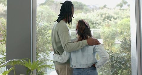 African American man and Indian woman standing, looking through glass toward lush garden