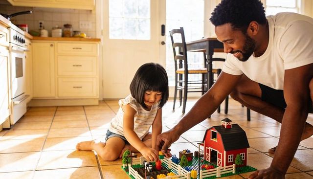 Father playing with daughter building colorful toy farm on sunlit kitchen floor