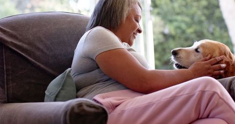 Smiling Woman Relaxing on Couch with Pet Dog Indoors