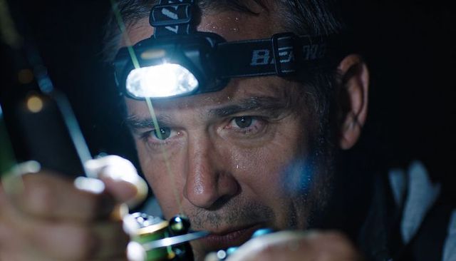 Fisherman adjusting reel under headlamp while night fishing, concentrating on line