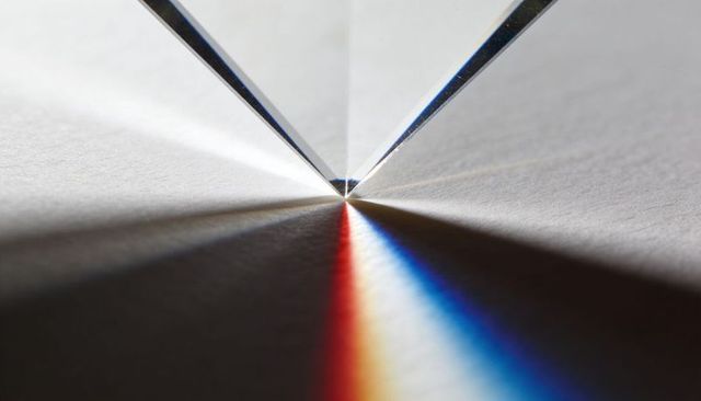 Prism apex refracting light into red and blue spectrum lines on folded paper macro tabletop