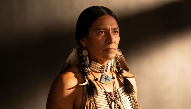 Indigenous man wearing traditional regalia, beadwork medallion, feather adornments, portrait