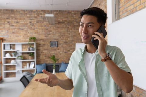 Professional Asian Man Calling Client in Modern Conference Room