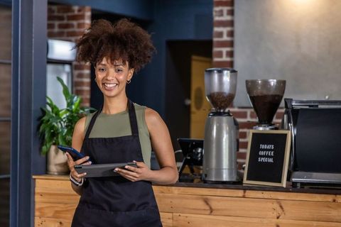 Smiling African American Barista Managing Tablet and Phone in Modern Coffee Shop
