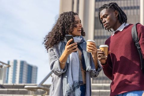 Diverse young professionals chatting on urban steps holding coffee cups and smartphone