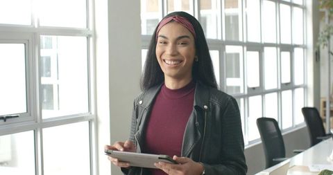 Smiling young professional in burgundy top holding tablet in bright coworking space