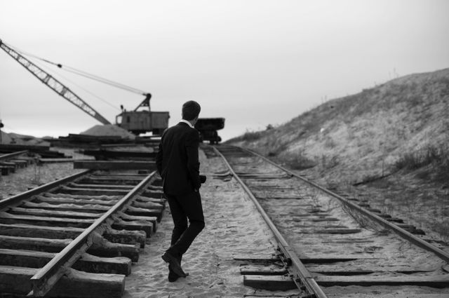 Businessman in a suit navigating a deserted railroad track. Scene evoking themes of solitude, determination, and transitions. Perfect for use in commercials, blogs, and articles discussing business journeys, career challenges, or illustrative metaphors in industrial contexts.