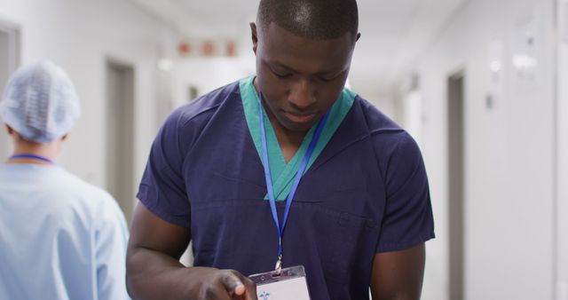 This image shows an African American nurse closely examining a badge while standing in a hospital hallway. Suitable for use in articles, medical education materials, healthcare recruitment websites, and advertisements emphasizing diversity and professionalism in the healthcare industry.