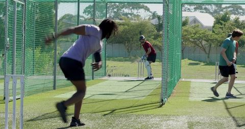 Cricket bowler delivering ball in outdoor practice nets with batter wearing helmet at crease