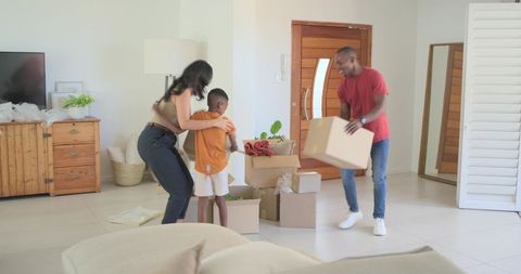 Family unpacking boxes in sunlit modern living room, arranging blankets and decor