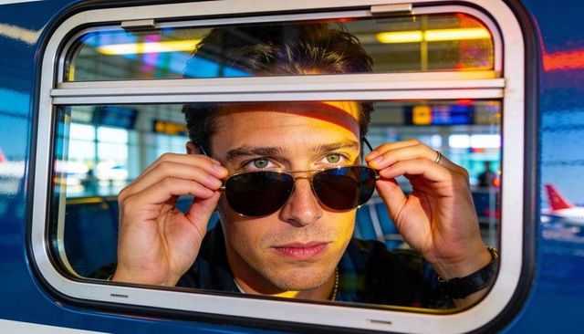 Lowering aviator sunglasses, man peering through aircraft window with colorful reflections