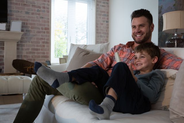 Father and son enjoying quality time together on a comfortable sofa in a cozy living room. Ideal for use in family-oriented advertisements, parenting blogs, lifestyle articles, and promotional materials for home decor or family entertainment products.