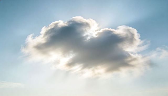 Glowing cumulus cloud radiating sun rays with silver lining and trailing cirrus in sky