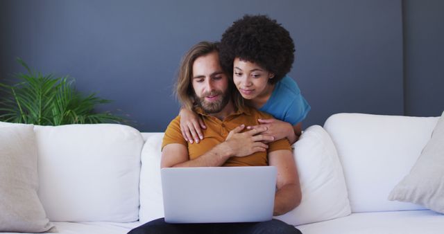 Biracial couple looking at laptop and embracing in living room. staying at home in self isolation during quarantine lockdown.