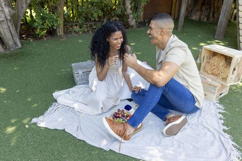Sunlit backyard picnic proposal laughing couple sharing toast while revealing jewelry box