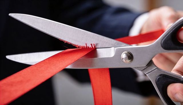 Hand cutting red ribbon with metal scissors during ribbon-cutting ceremony close-up