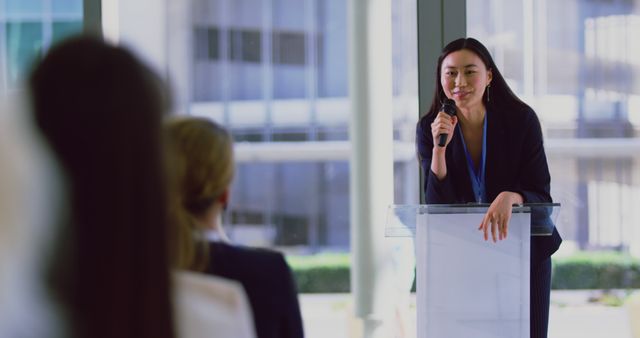Young woman giving presentation with microphone, engaging with audience. Suitable for illustrating corporate training, leadership talks, motivational speeches, professional conferences, or business-related educational materials.