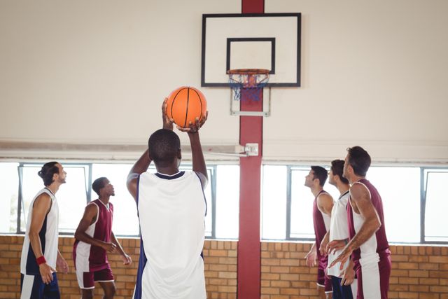 Basketball player taking a free throw shot in an indoor court with teammates and opponents watching. Ideal for use in sports articles, athletic training materials, teamwork promotions, and fitness blogs.