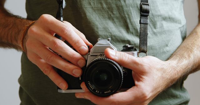 This image captures a close-up view of a man holding a vintage camera, highlighting the details and design of the camera and the man's concentration. It is ideal for use in hobby photography websites, vintage camera promotions, and articles related to photography tips and techniques. Great for illustrating a passion for photography or the resurgence of interest in film cameras.