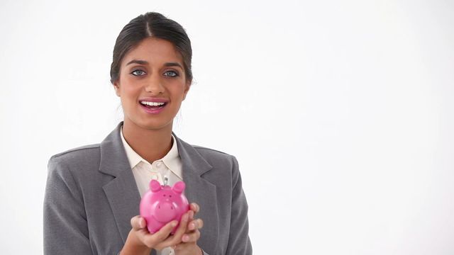 Professional woman in a suit holding a piggy bank, symbolizing savings and financial growth. Suitable for financial services advertisements, investment guides, money management tutorials, corporate training materials, and articles on personal finance or business success.