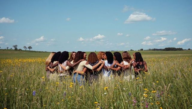 Women linking arms in wildflower meadow embracing sisterhood, unity and friendship