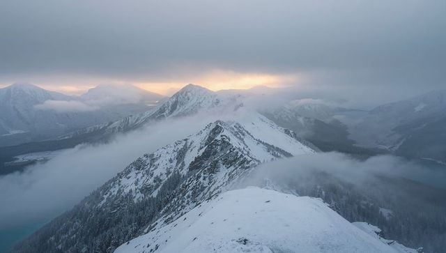 Stretching snowy alpine ridge cutting through mist with alpenglow warming turquoise lake