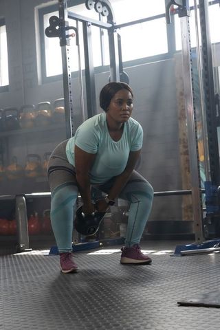 African american woman lifting kettlebell for strength training in industrial gym, focused