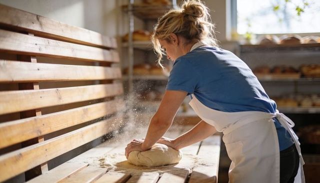 Baker kneading dough on rustic wooden bench in sunlit artisan bakery
