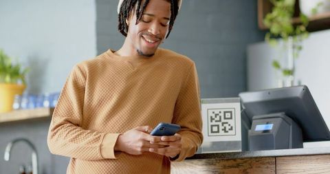 African American young man using smartphone at cafe counter with QR code payment