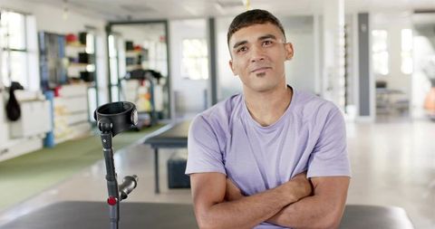 Confident man standing in sunlit rehabilitation gym with elbow crutch and crossed arms