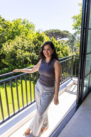 Smiling woman standing barefoot on sunny balcony overlooking lush garden and lawn
