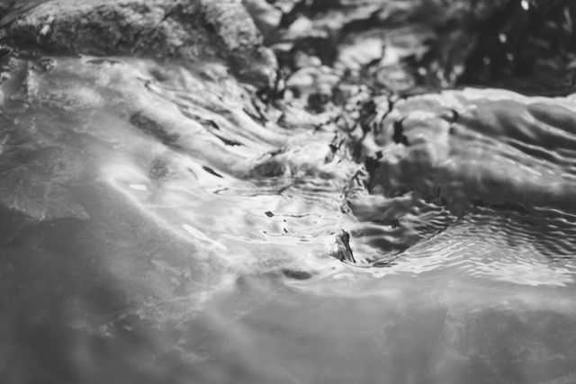 Black and white closeup of water surface with rippling texture. Useful for backgrounds, artistic projects, or nature-themed designs. Suggesting a calm and flowing water motion.