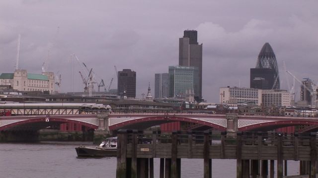 Panoramic view of London's skyline on an overcast day, showcasing modern and historic architecture. Includes iconic buildings like the Gherkin and a prominent bridge over River Thames. Ideal for use in articles about London, urban environments, weather, construction, or architecture.