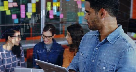 Business analyst holding laptop analyzing financial charts, team collaborating in office