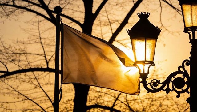 Translucent flag waving at sunset catching sunlight by ornate street lantern silhouette
